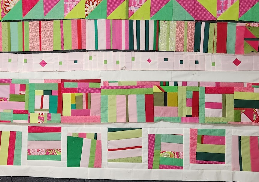 A pink and green in-progress quilt top set in rows, some of which have white sashing.