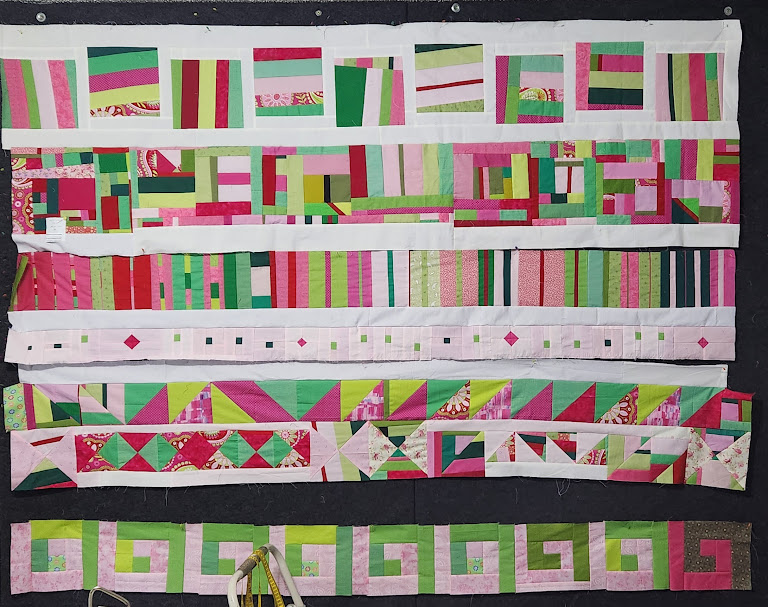 The pink and green in-progress quilt top set in rows, most of which are separated with white sashing.