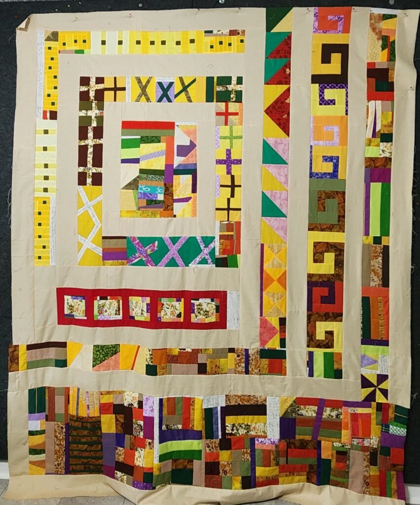 The same completed improv medallion-type quilt top using oranges, greens, yellows, purples, and browns with minor changes