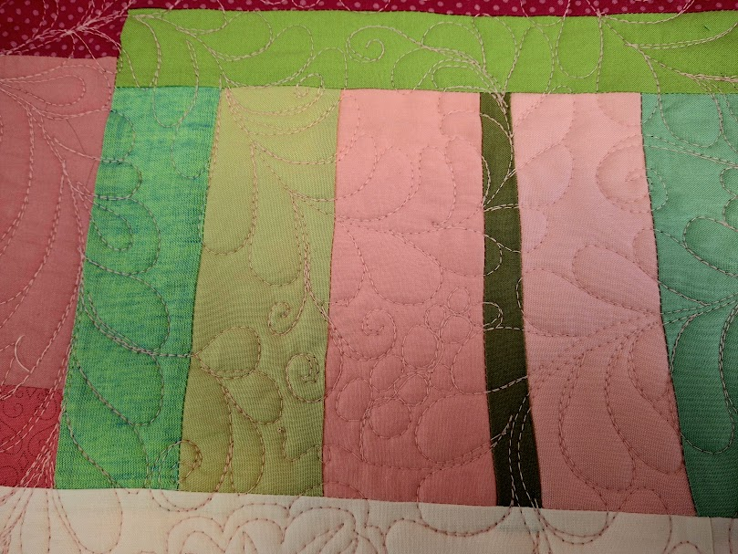 Picture of improv quilt in red, pink, green. Improv quilting of feathers, scrolls, and flowers. 