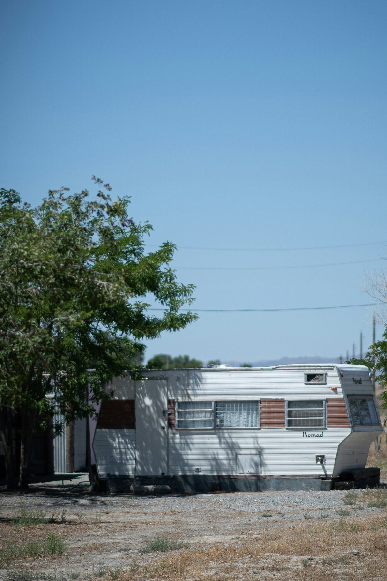 Photo of an old trailer house partial hidden behind a tree. Used aa a hint to the sequel of This World So Fierce.