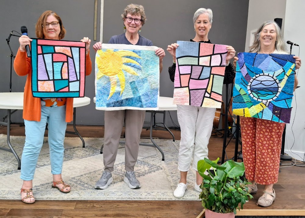 Four of my Pensacola students holding up their stained-glass quilts from the workshop the previous day.