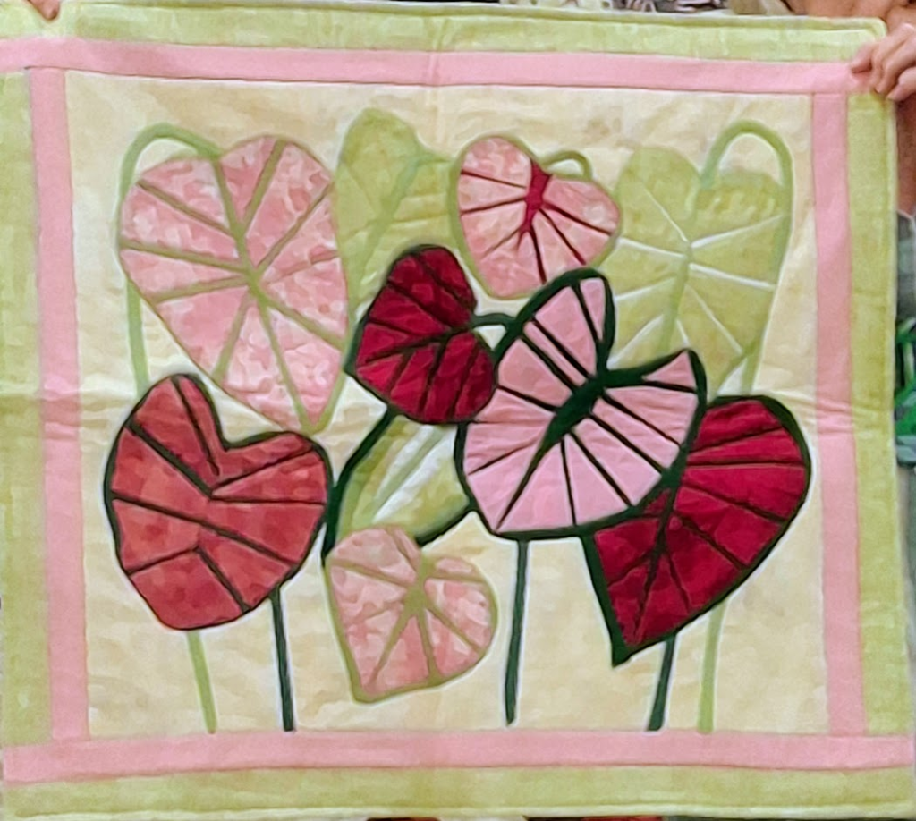 A wall-hanging in beautiful modern colors of pink, red, and green caladium leaves appliqued on it.